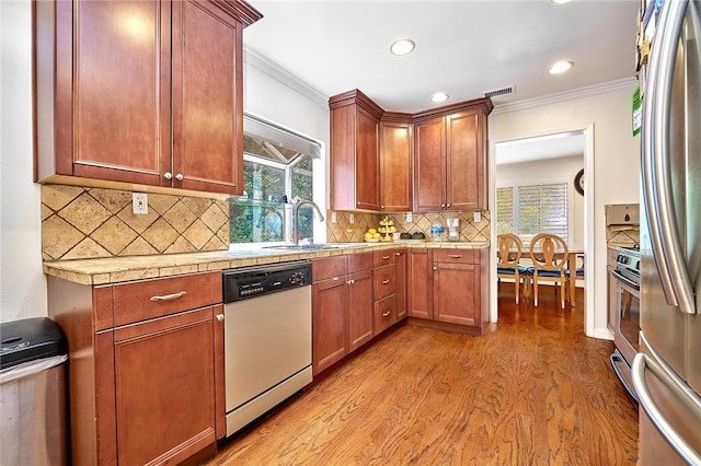 kitchen with appliances with stainless steel finishes, light countertops, crown molding, light wood-type flooring, and a sink