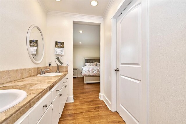 ensuite bathroom featuring crown molding, a sink, and wood finished floors