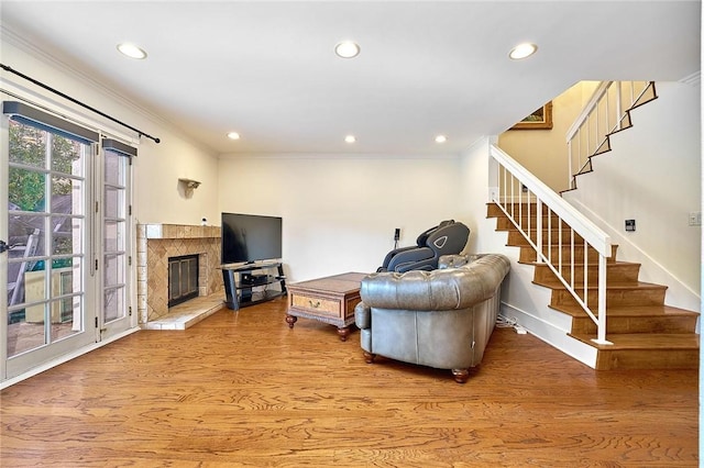 living area featuring recessed lighting, stairway, light wood-style flooring, ornamental molding, and a glass covered fireplace