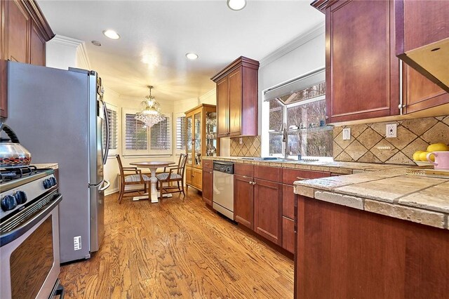 kitchen featuring tasteful backsplash, appliances with stainless steel finishes, an inviting chandelier, crown molding, and light wood-type flooring