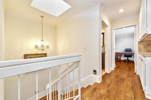 hall with a skylight, light wood-style floors, ornamental molding, an upstairs landing, and baseboards