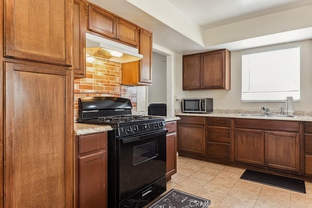 kitchen featuring black gas range, tasteful backsplash, stainless steel microwave, under cabinet range hood, and a sink