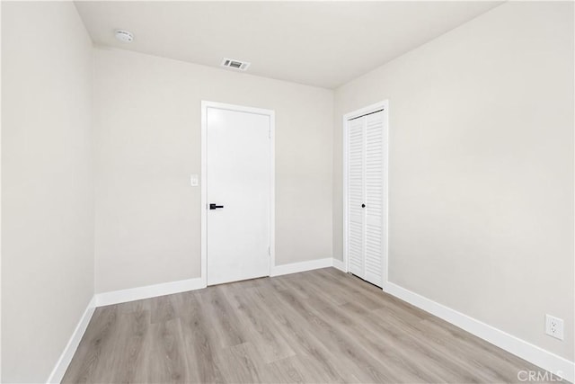 unfurnished bedroom featuring light wood-style flooring, a closet, visible vents, and baseboards