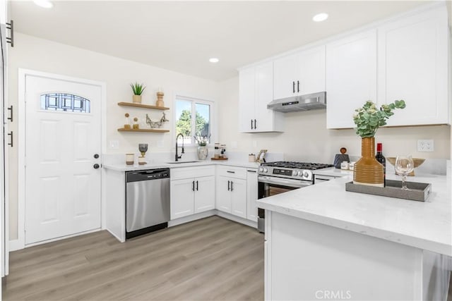 kitchen featuring stainless steel appliances, light wood-type flooring, under cabinet range hood, white cabinetry, and a sink