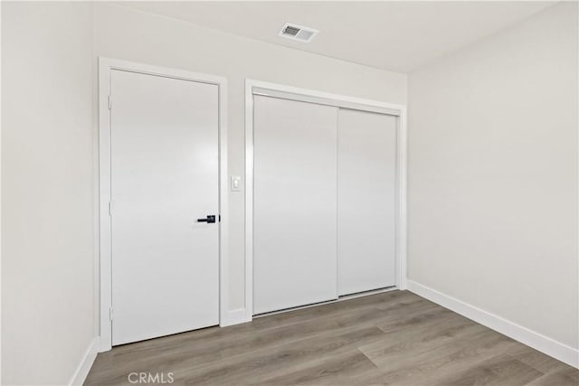 unfurnished bedroom featuring a closet, wood finished floors, visible vents, and baseboards