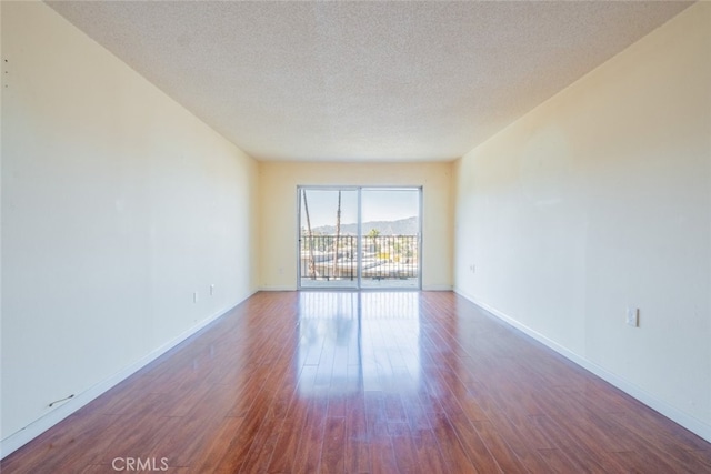 unfurnished room with a textured ceiling, baseboards, and wood finished floors