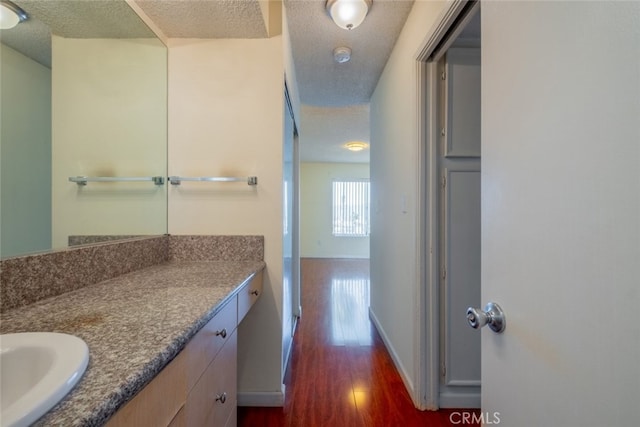 bathroom with a textured ceiling, vanity, baseboards, and wood finished floors