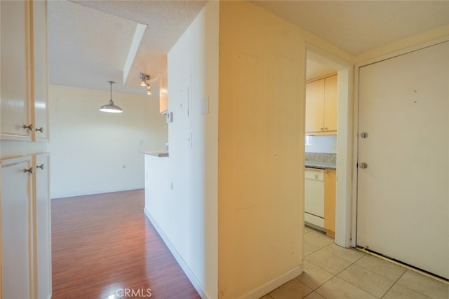 hall featuring light tile patterned floors, baseboards, and a textured ceiling