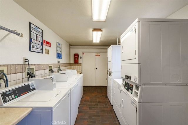 common laundry area featuring washing machine and dryer, stacked washer / drying machine, and brick floor