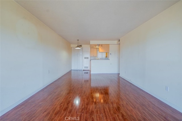 unfurnished living room featuring visible vents, baseboards, and wood finished floors