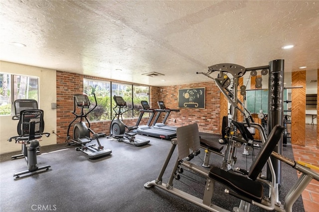 workout area with visible vents, a textured ceiling, and brick wall