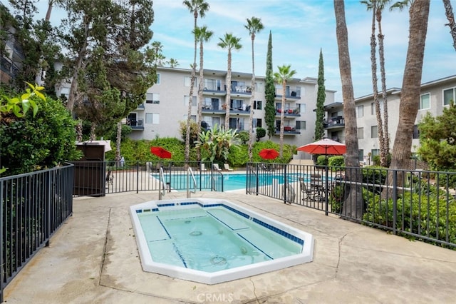 community pool with a community hot tub, a patio, and fence