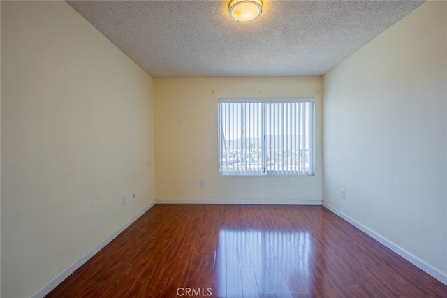 empty room with baseboards, a textured ceiling, and wood finished floors