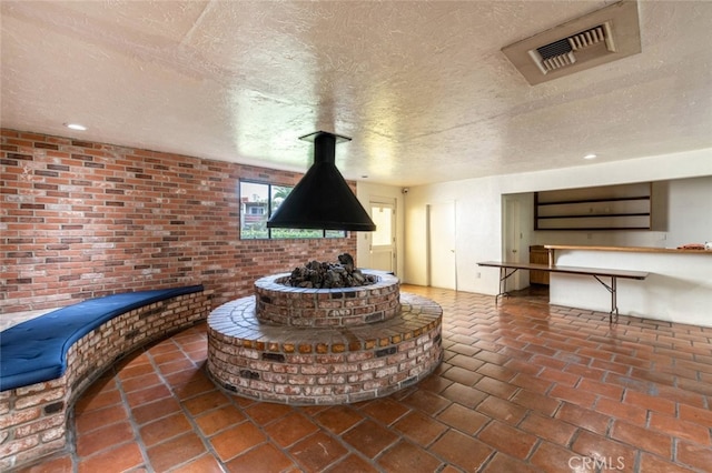 living area with visible vents, brick wall, and a textured ceiling