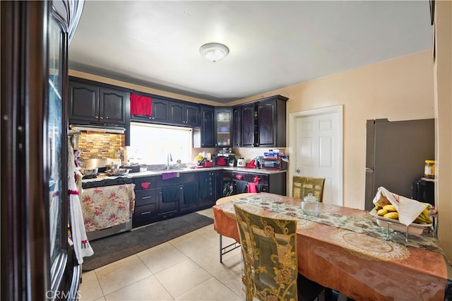 kitchen with light tile patterned floors, freestanding refrigerator, a sink, light countertops, and gas range