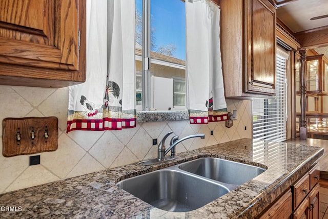 kitchen featuring tasteful backsplash, dark stone counters, brown cabinets, and a sink