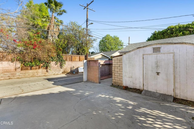 view of gate with a storage shed, a patio area, an outdoor structure, and fence