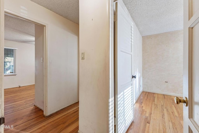 hall with a textured ceiling and light wood finished floors