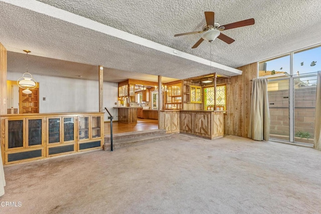 carpeted spare room with a textured ceiling, ceiling fan, wood walls, and bar area