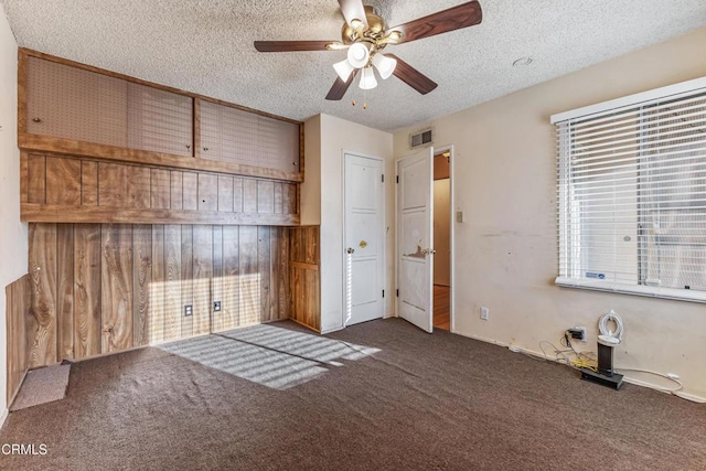 unfurnished bedroom with a textured ceiling, carpet flooring, visible vents, and wooden walls