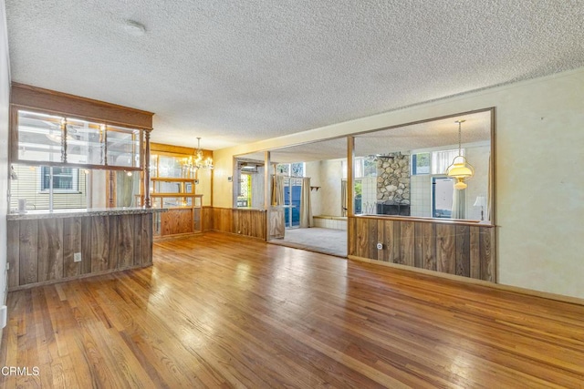 unfurnished living room with a chandelier, a textured ceiling, wooden walls, and wood finished floors