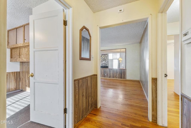 hallway featuring a textured ceiling, a wainscoted wall, wood finished floors, and wooden walls