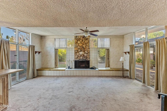 unfurnished living room with carpet floors, plenty of natural light, a textured ceiling, and a stone fireplace