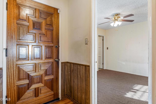 hall featuring carpet, wooden walls, a textured ceiling, and wainscoting