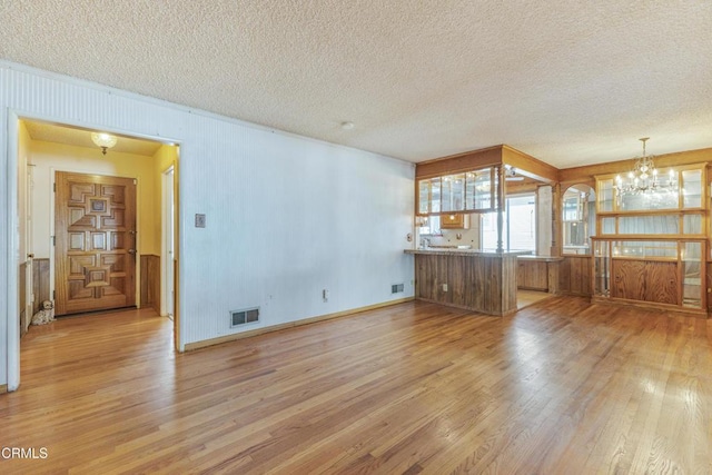 unfurnished living room featuring visible vents, a notable chandelier, a textured ceiling, and wood finished floors