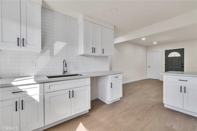 kitchen with light countertops, light wood-type flooring, white cabinets, and a sink