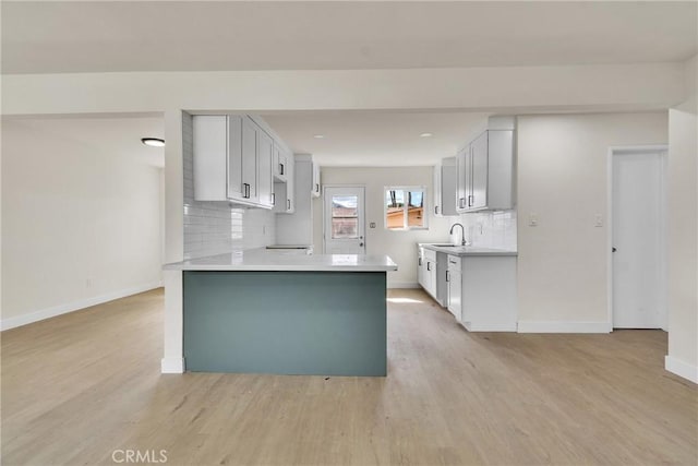 kitchen featuring baseboards, light countertops, a sink, and light wood-style floors