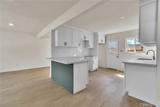 kitchen with baseboards, decorative backsplash, white cabinets, light wood-type flooring, and a sink