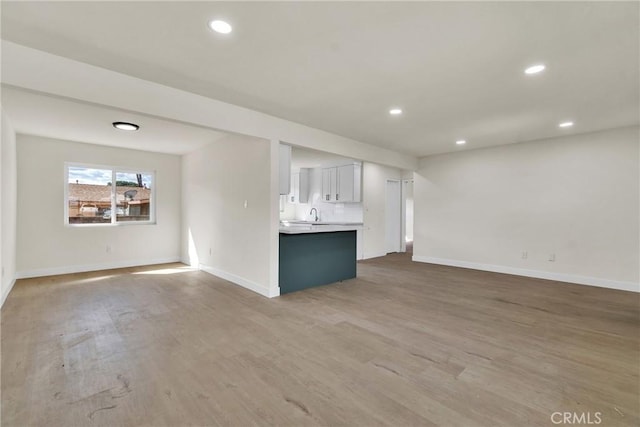 unfurnished living room with baseboards, a sink, wood finished floors, and recessed lighting