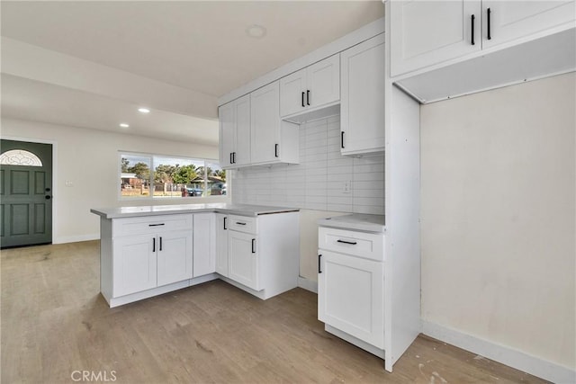 kitchen featuring light wood-type flooring, tasteful backsplash, a peninsula, and white cabinetry