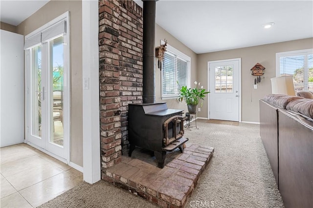 interior space with light carpet, light tile patterned floors, a wood stove, and baseboards