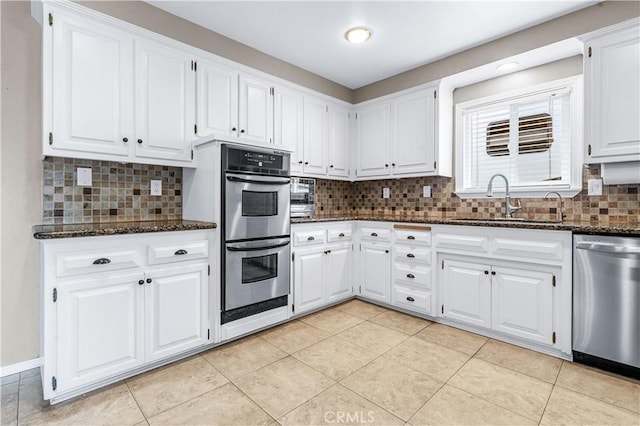 kitchen with stainless steel appliances, dark stone countertops, backsplash, and white cabinetry