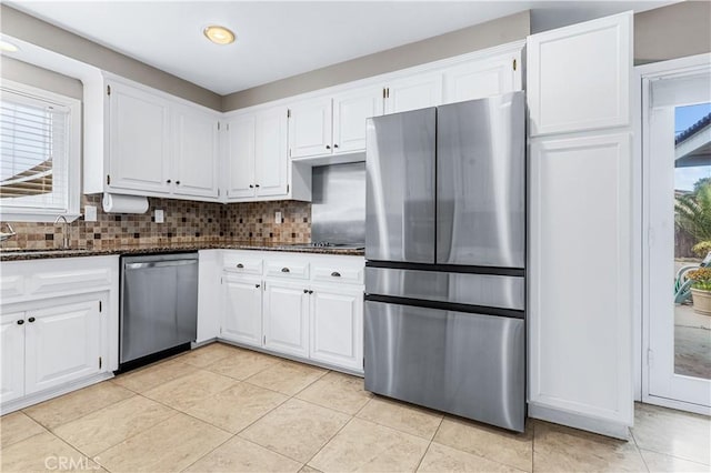 kitchen featuring stainless steel appliances, decorative backsplash, white cabinets, a sink, and dark stone counters