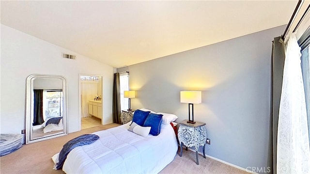 bedroom featuring light colored carpet, visible vents, vaulted ceiling, and ensuite bath