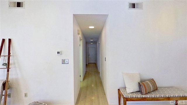 hall with light wood-type flooring, visible vents, and baseboards