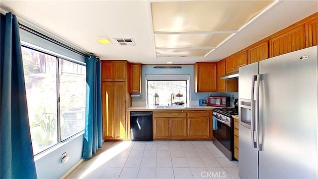 kitchen featuring under cabinet range hood, stainless steel appliances, a sink, light countertops, and brown cabinetry