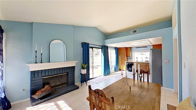 dining room featuring lofted ceiling, light tile patterned floors, visible vents, baseboards, and a brick fireplace