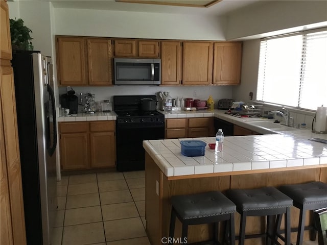 kitchen featuring light tile patterned floors, stainless steel appliances, a peninsula, a sink, and tile counters