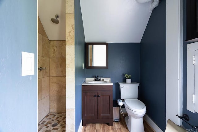 bathroom with tiled shower, lofted ceiling, toilet, wood finished floors, and vanity