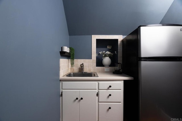 kitchen with a sink, white cabinetry, light countertops, freestanding refrigerator, and tasteful backsplash