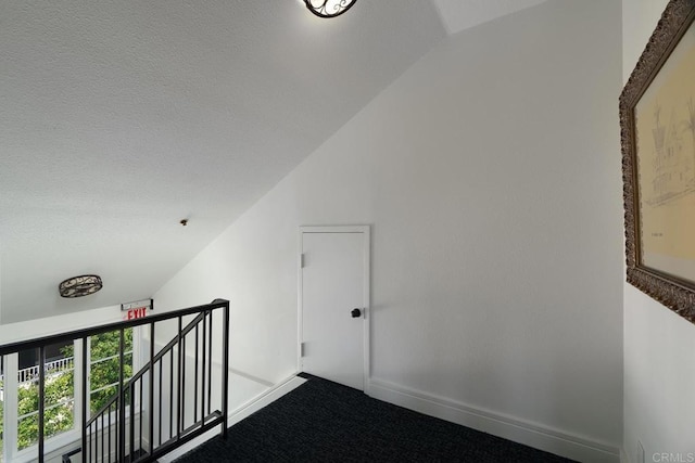 interior space featuring an upstairs landing, dark colored carpet, vaulted ceiling, and baseboards