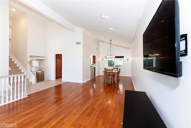 unfurnished living room with high vaulted ceiling, wood finished floors, visible vents, stairs, and beam ceiling