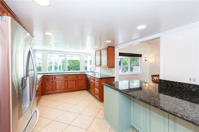 kitchen with light tile patterned floors, stainless steel appliances, a sink, brown cabinets, and dark stone countertops