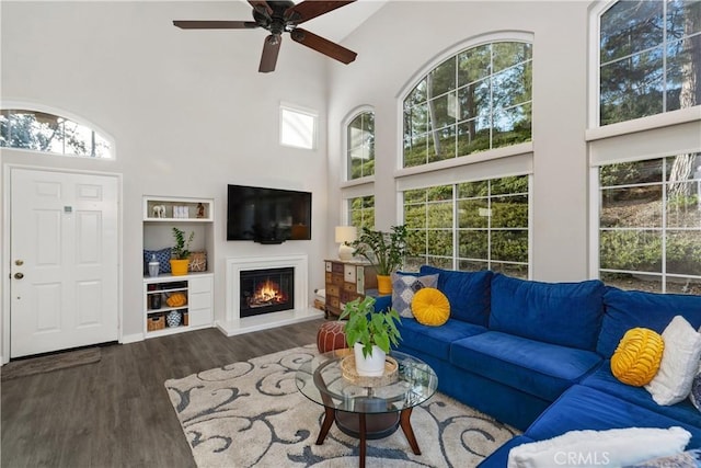 living area with a high ceiling, a ceiling fan, wood finished floors, and a glass covered fireplace