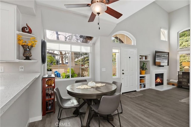 dining space featuring ceiling fan, high vaulted ceiling, a glass covered fireplace, and wood finished floors