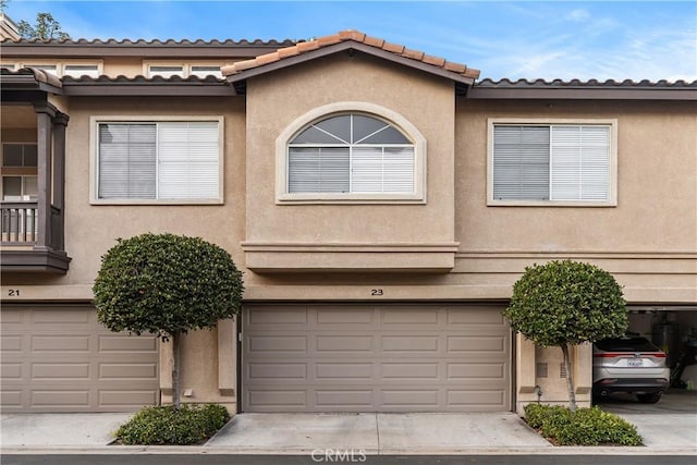 townhome / multi-family property featuring a garage, concrete driveway, a tile roof, and stucco siding